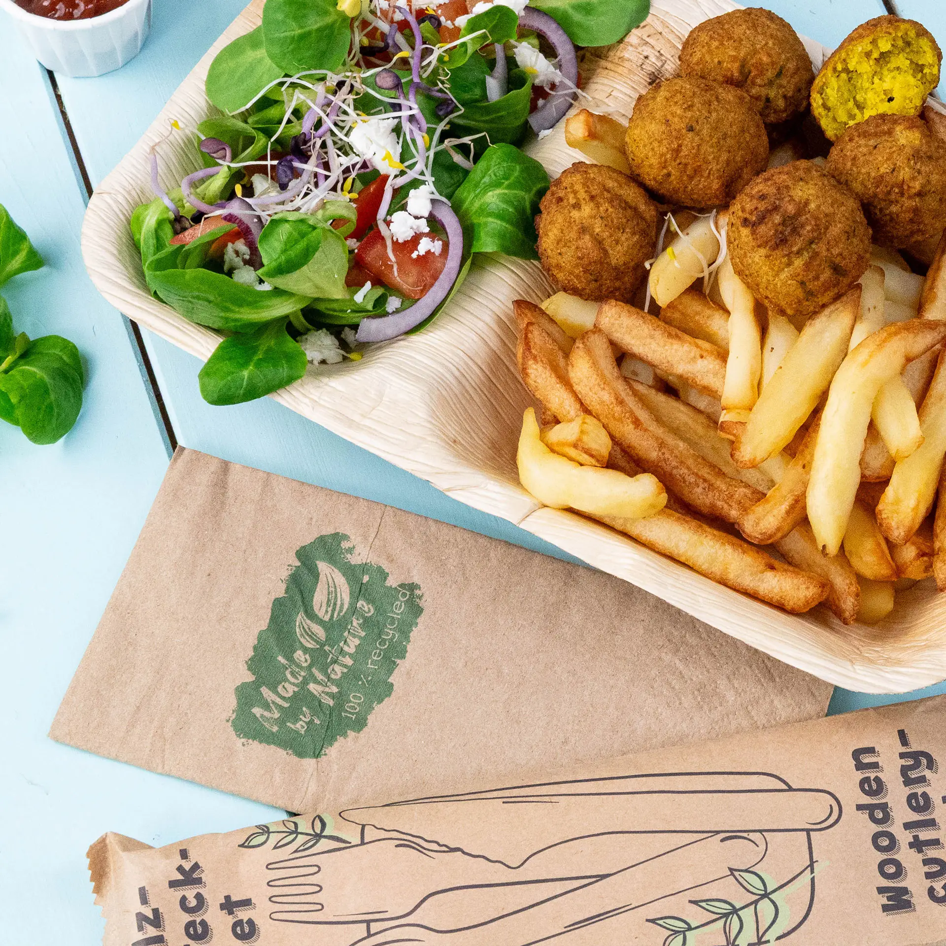 One plate featuring falafel balls, fries, and salad; with a paper napkin labeled "Made by Nature" next to wooden cutlery.