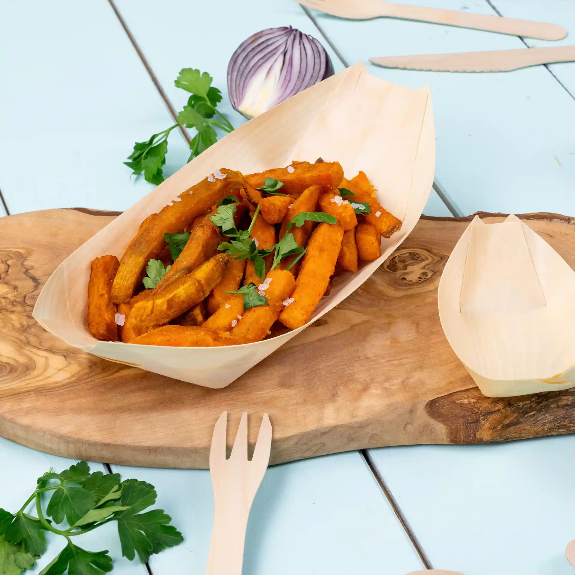 Wooden boat-shaped serving dish with sweet potato fries, garnished with parsley, on a wooden surface.