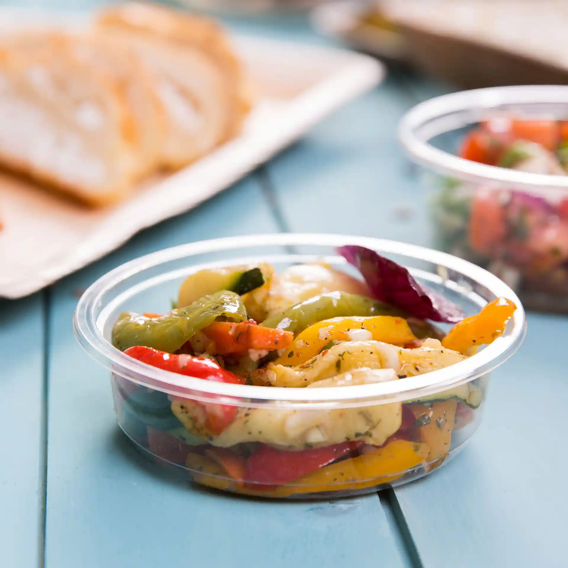 Transparent round deli container with mixed vegetables, placed on a blue wooden surface.