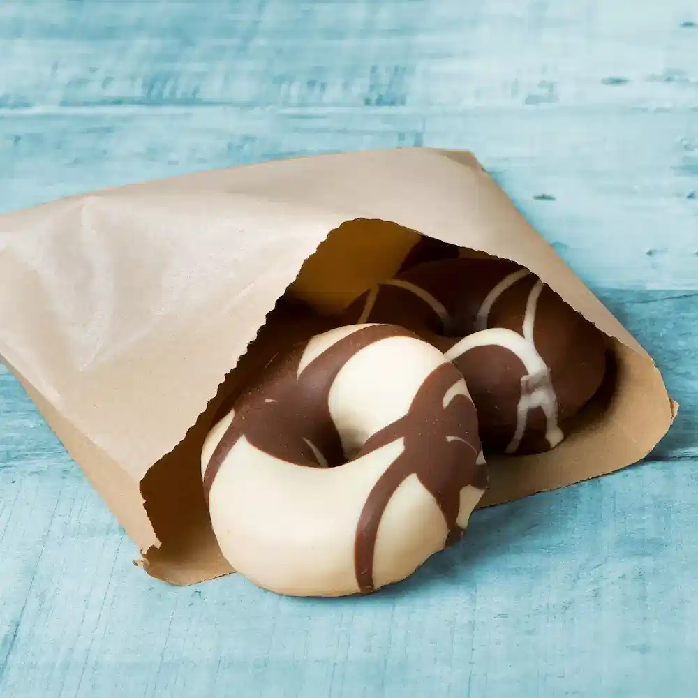 Chocolate-covered donuts partially visible in a brown paper bag on a blue wooden surface.