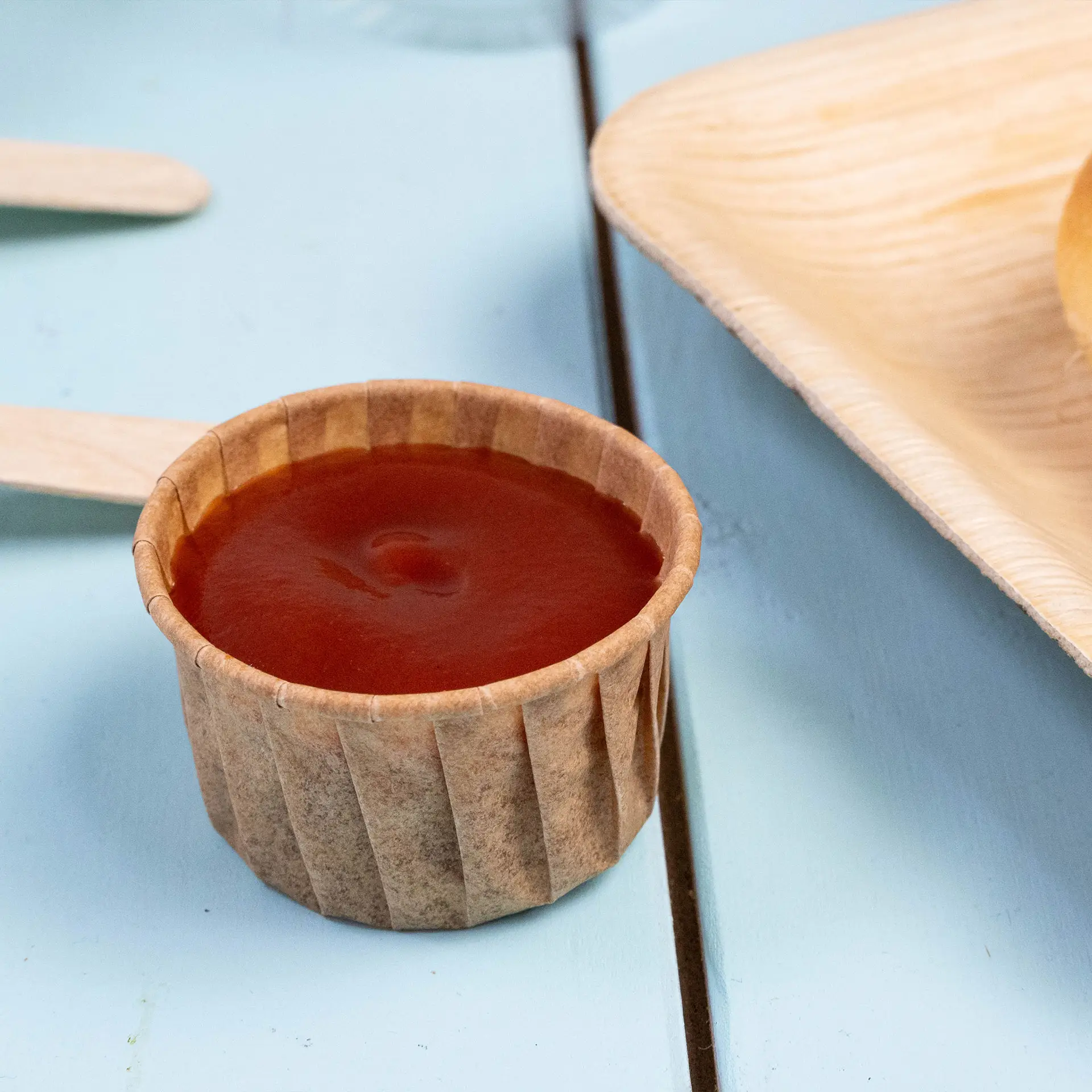 Brown paper cup filled with sauce, suitable for dips and small servings, on a blue table surface.