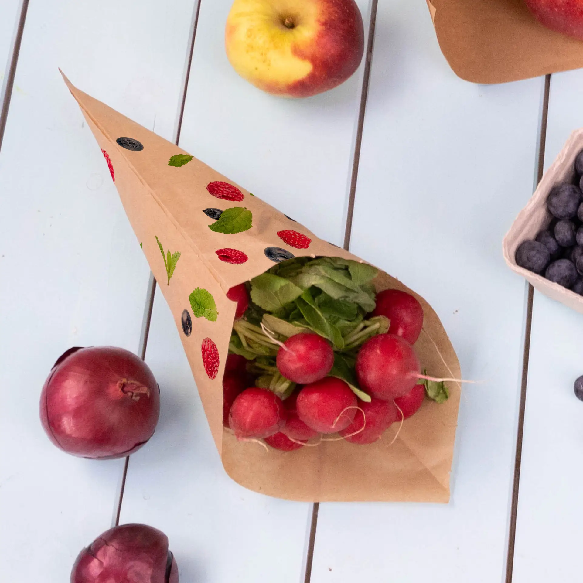 Brown paper cone bag filled with radishes and herbs, surrounded by apples, red onions, and blueberries on a light surface.