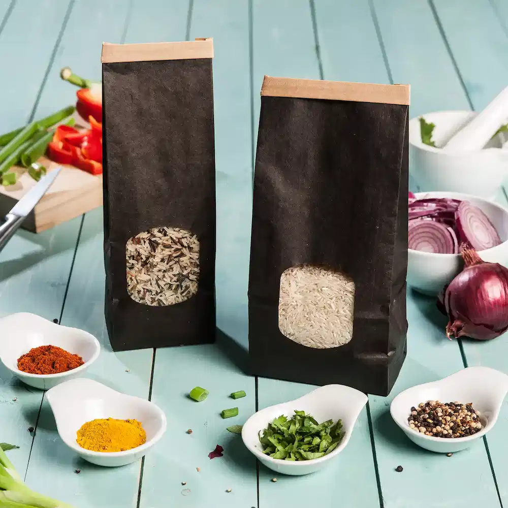 Two black block bottom bags containing rice and a mix of herbs and spices, surrounded by small bowls of seasoning.