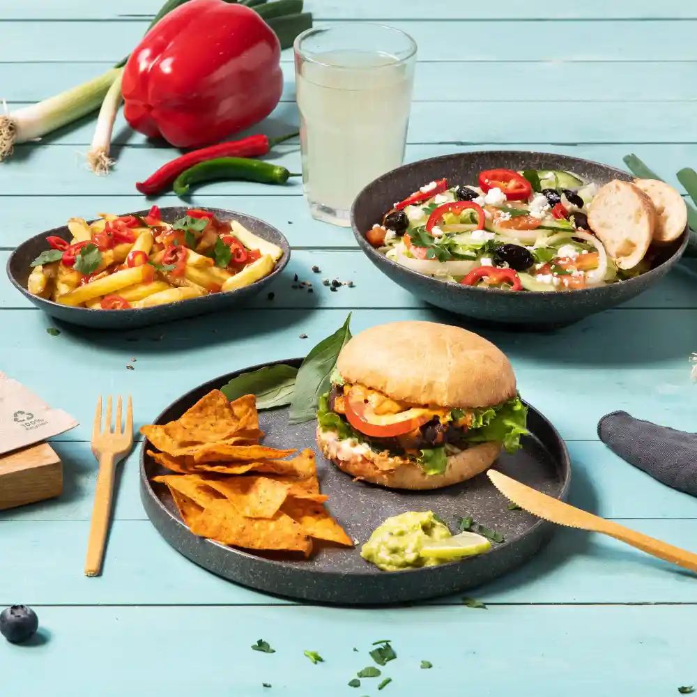 A burger with lettuce, tomato, and sauce, served with tortilla chips and guacamole, alongside a salad and fries.