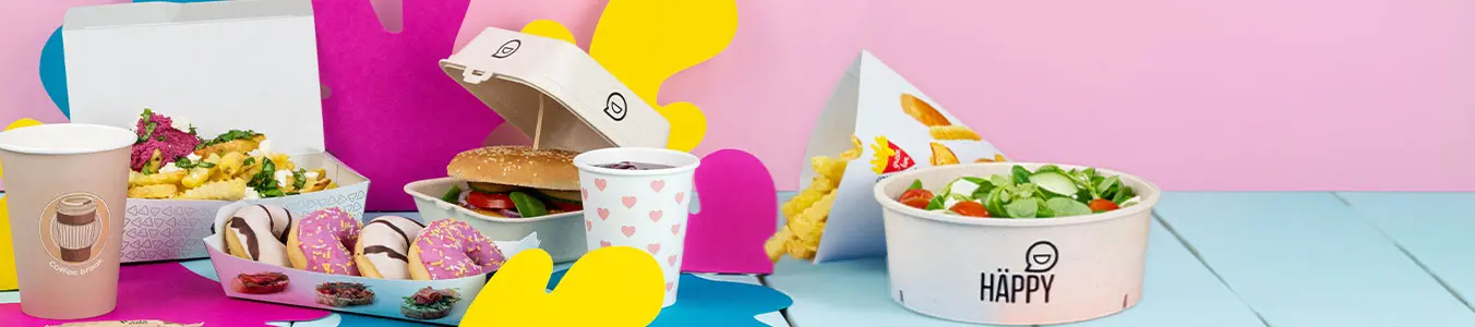 Takeaway fast food arrangement with a burger, fries, colorful salad bowl, sauce, and a drink on a blue surface.