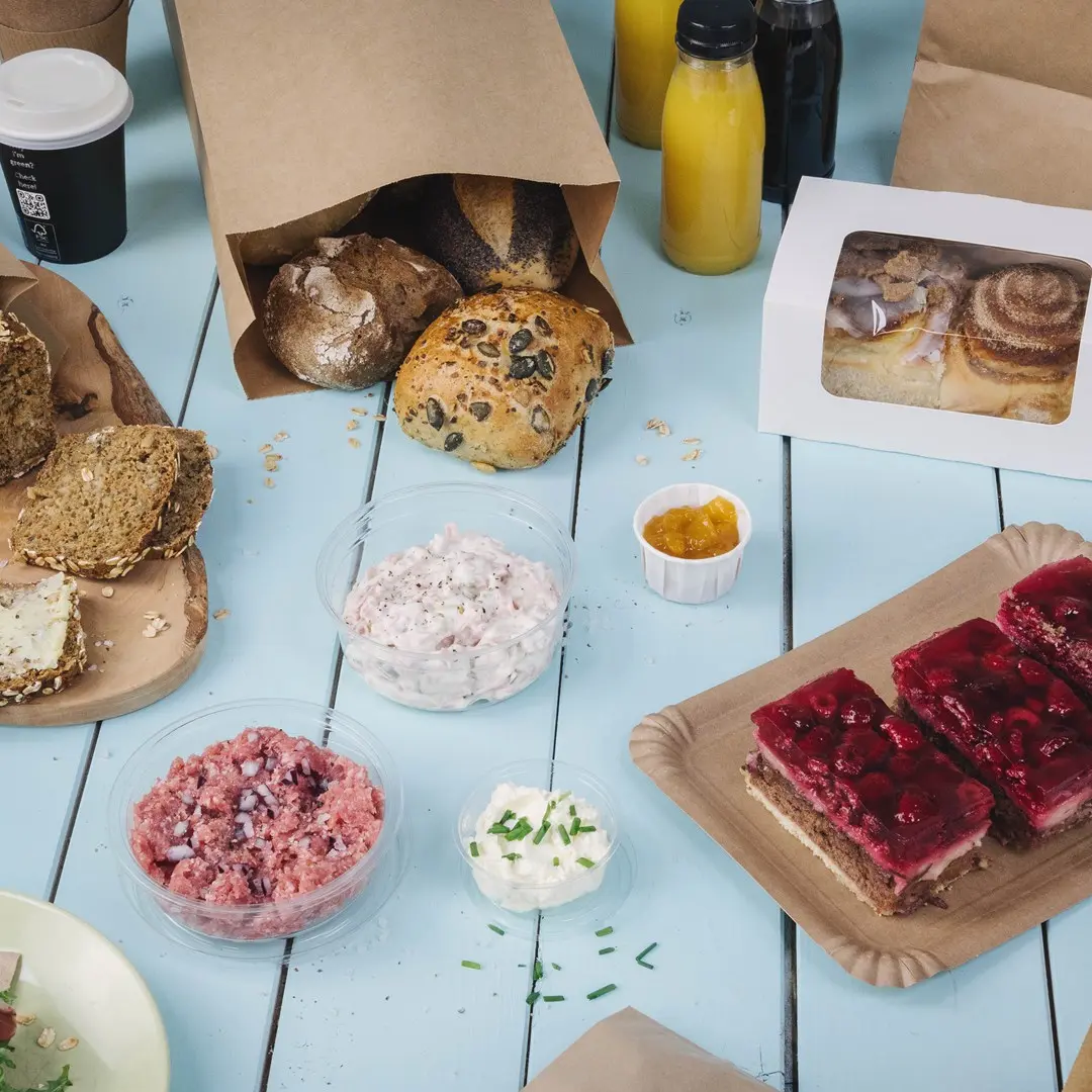 Assorted baked goods including rolls, spreads, desserts, and beverages on a blue wooden table.