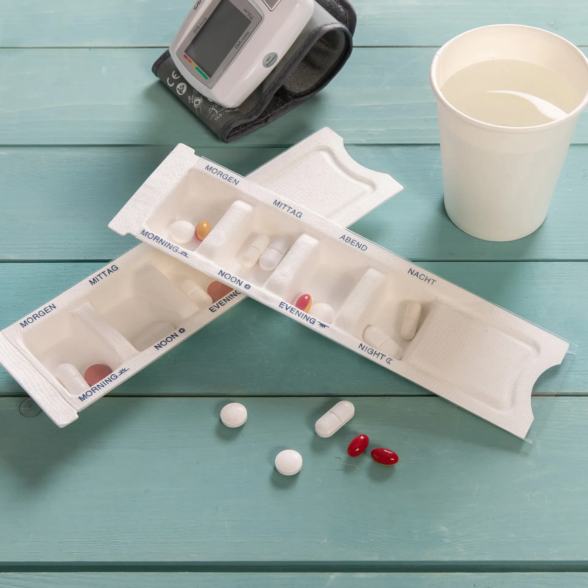 A biodegradable medication dispenser with compartments for morning, noon, evening, and night; includes pills and a cup of water.